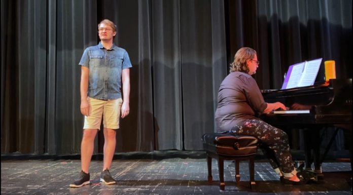 Graduate performs ‘Beautiful City’ from ‘Godspell’ Man stands on stage next to piano