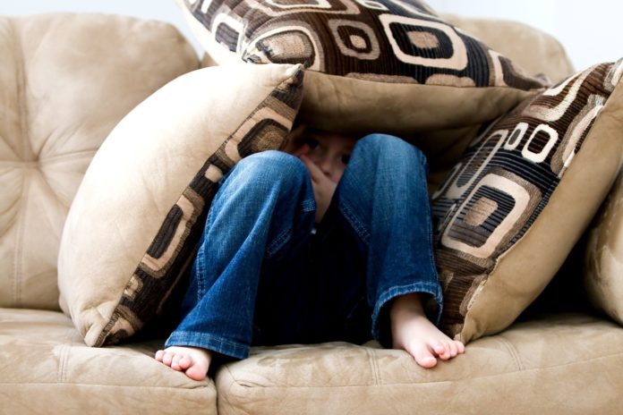 child on couch covering up with pillows