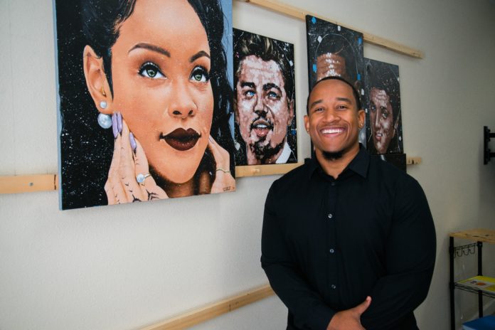Caleb Brown stands in front of his paintings