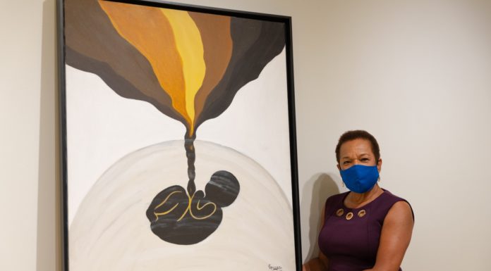 Alumna denied exhibition in ’70s finally gets to show her art Woman stands next to painting