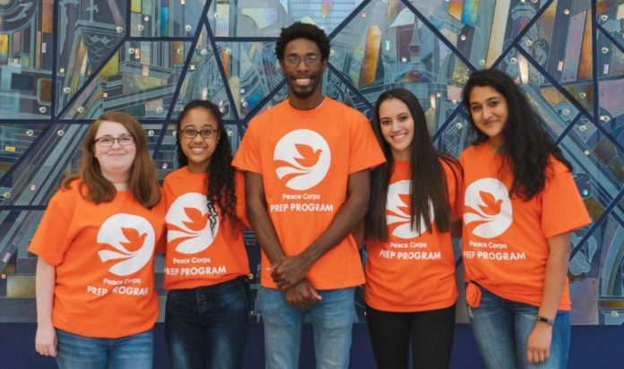 Five students smile at the camera while wearing orange Peace Corps Prep program T-shirts