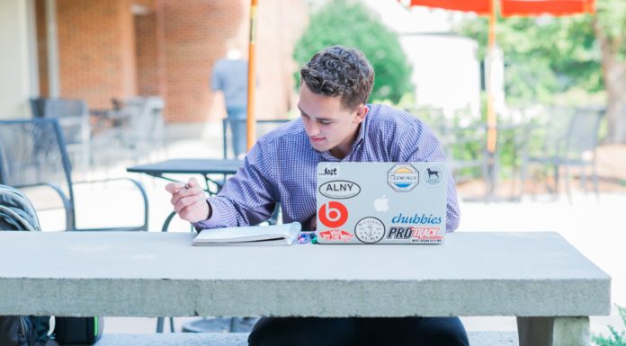 How to prepare for course registration and maximize time with your adviser | Ask Kelly Male student sits at a table outside. He has a laptop in front of him and is writing in a notebook.