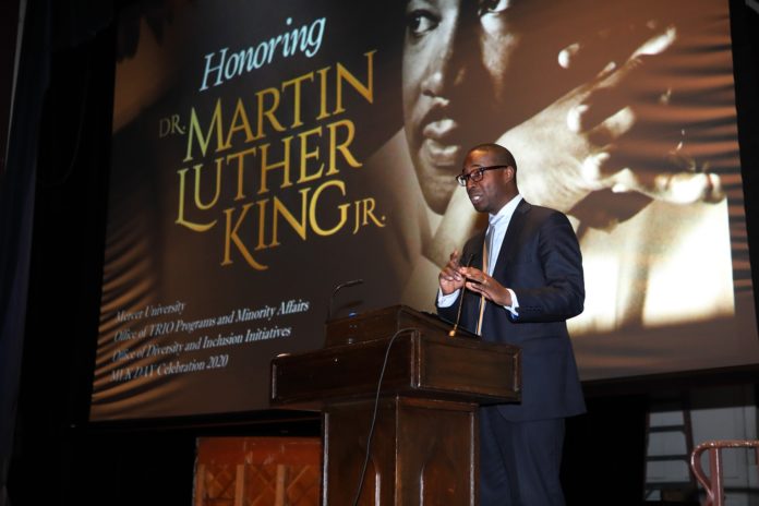 Man stands behind podium. Projected on the screen behind him is a photo of Martin Luther King Jr. and the words Honoring Dr. Martin Luther King Jr.