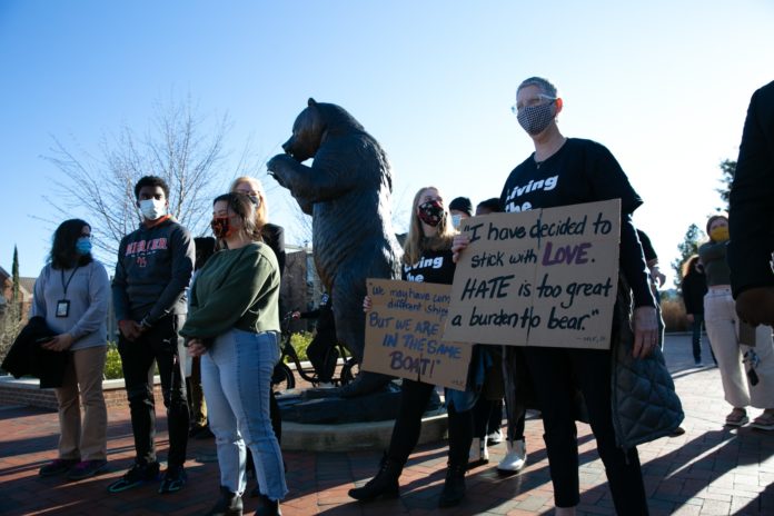 Masked people gather around a bear statue holding signs for social justice