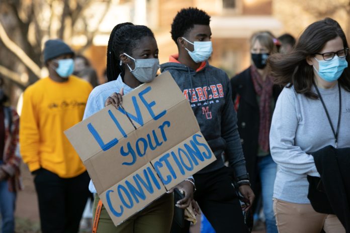 Woman holds a cardboard sign that says Live your Convictions