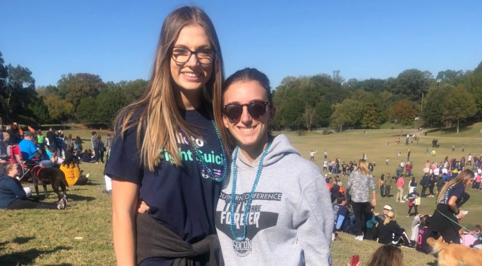 Student hopes suicide prevention walk will help break stigma around mental health Two women dressed in athletic clothing and wearing beads stand in a park full of people