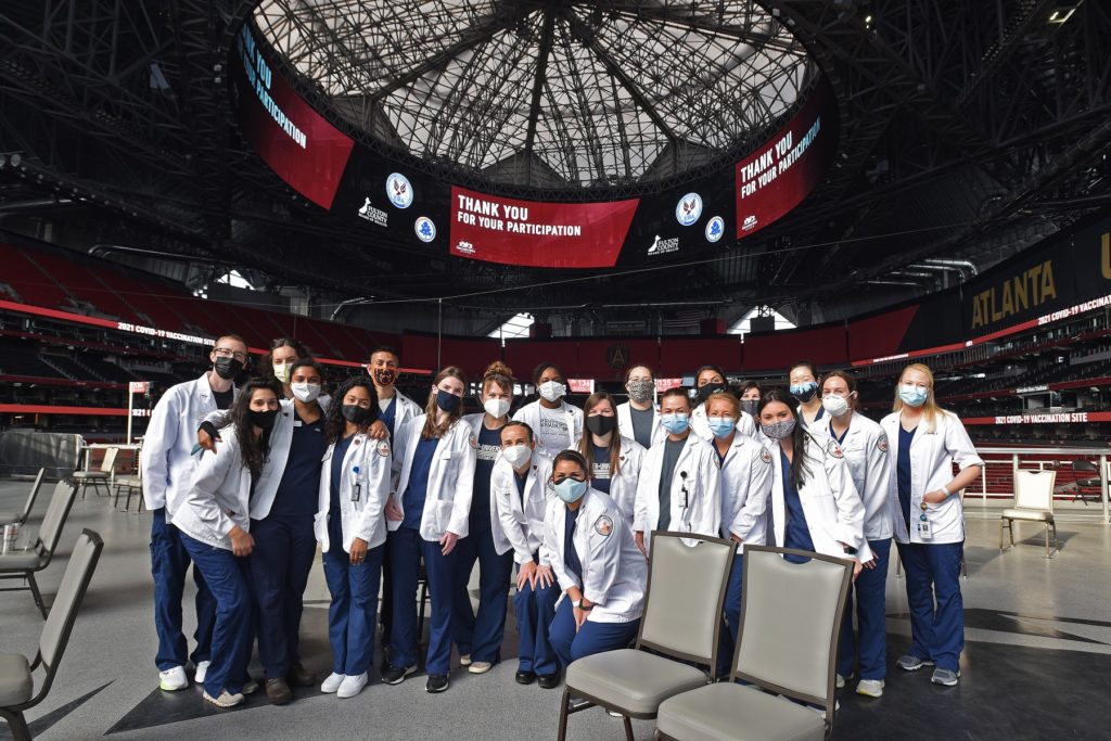 A group of students in lab coats stand under the dome at Mercedes-Benz Stadium