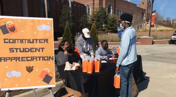 Mercer helps commuter students find community on campus A table is set up outside next to a sign that says commuter student appreciation. three people behind the table hand out a gift back to a student standing in front of the table