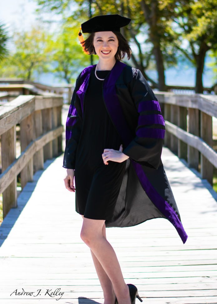 A woman dress in law graduation regalia stands on a wood bridge