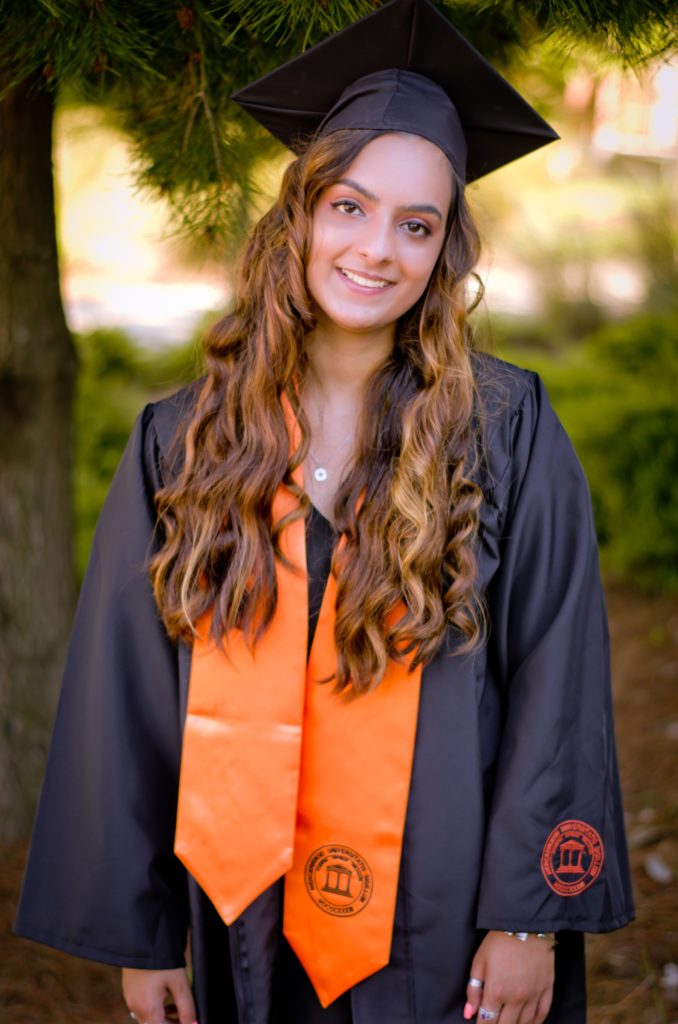 A graduate wears cap, gown and orange stole