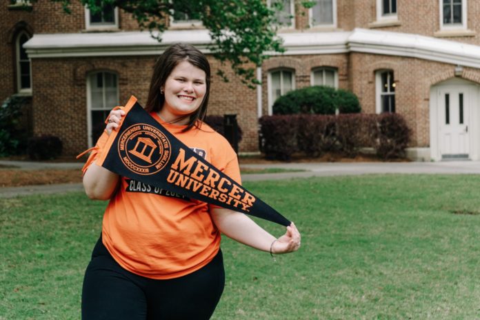 A woman wearing an orange shirt smiles while holding a Mercer pennant.