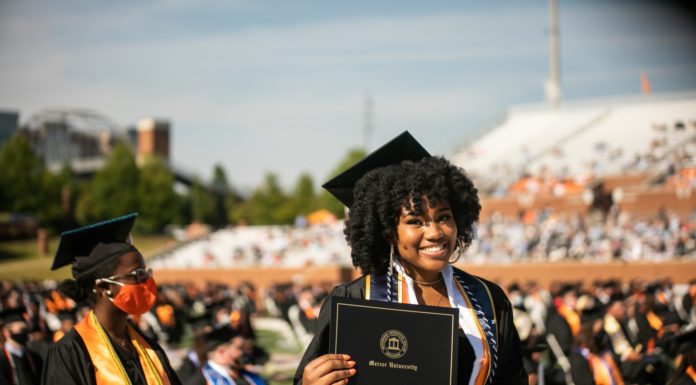 Watch graduation video recap and download commencement photos a smiling graduate wearing a black cap and gown holds her mercer university diploma