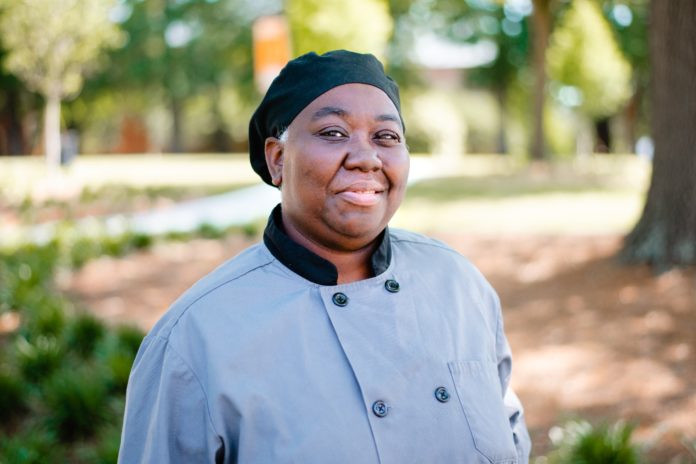 A woman wearing a chef's coat smiles