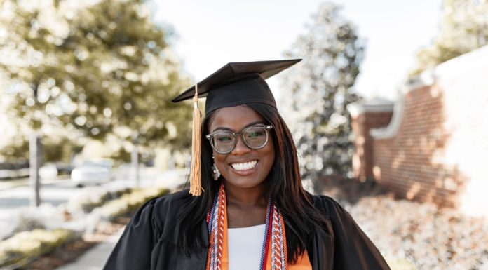 Graduate Spotlight: Erinn McGuire A woman stands on a sidewalk wearing a graduation cap and gown, plus cords and orange stole