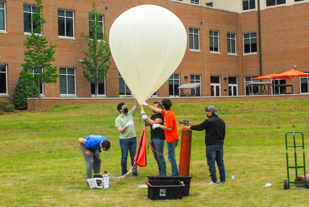 Students gather around a giant balloon in a grassy field