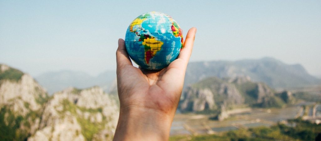 a hand holds a globe in front of mountains