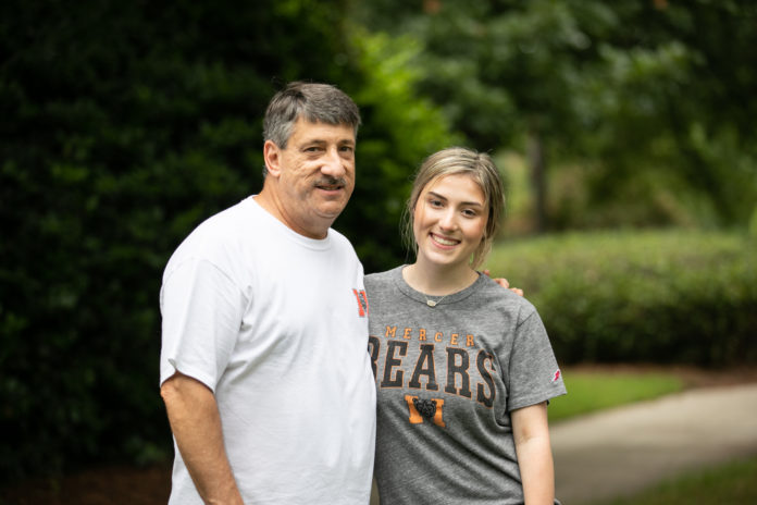 father and daughter pose for a picture in front of greenery