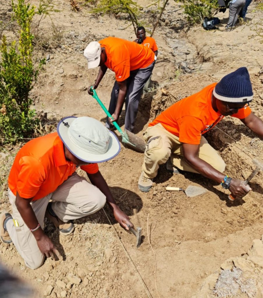 three men wearing orange shirt at an archaeological dig