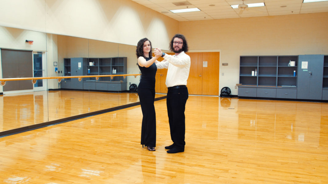 A man and woman face each other holding hands as they prepare to dance