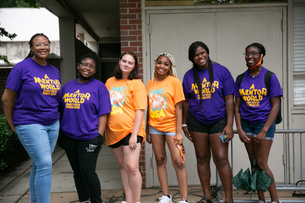 students in orange and purple shirts stand in front of a building