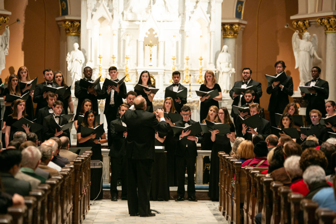 A conductor leads a choir in front of a church