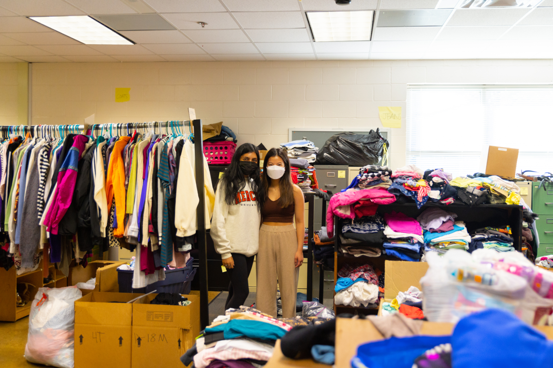 Two students stand among a room full of clothes