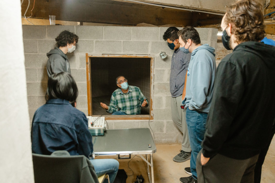 a professors sits inside a reverb chamber and talks to students on the outside