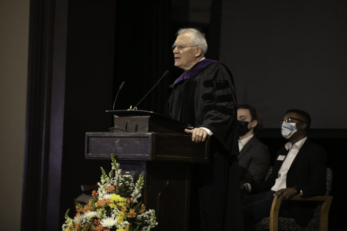 Man wearing black robe stands behind podium.
