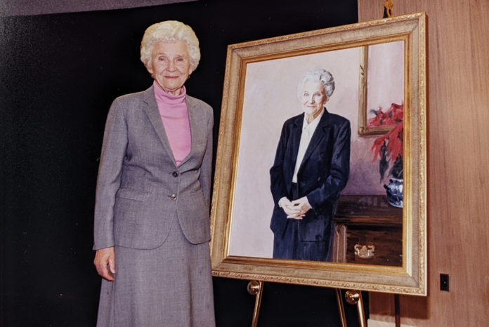 A woman stands next to a portrait of herself