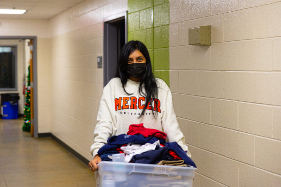 A young woman wearing a Mercer shirt carries a bin of clothes