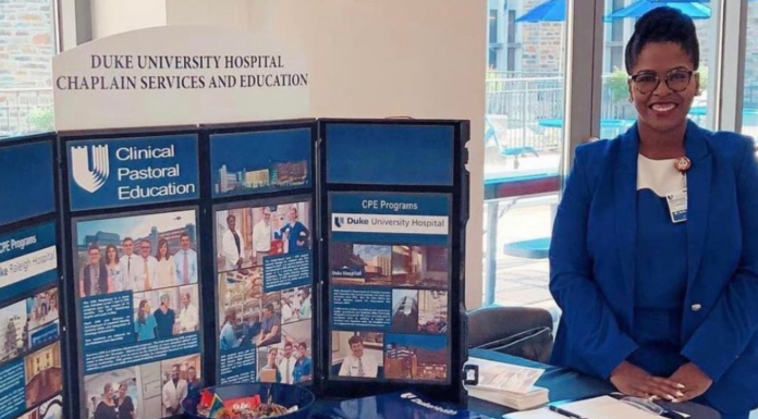 Theology alumna called to listen in times of crisis A woman wearing a blue suit stands next to a trifold board that says Duke University Hospital Chaplain Services and Education
