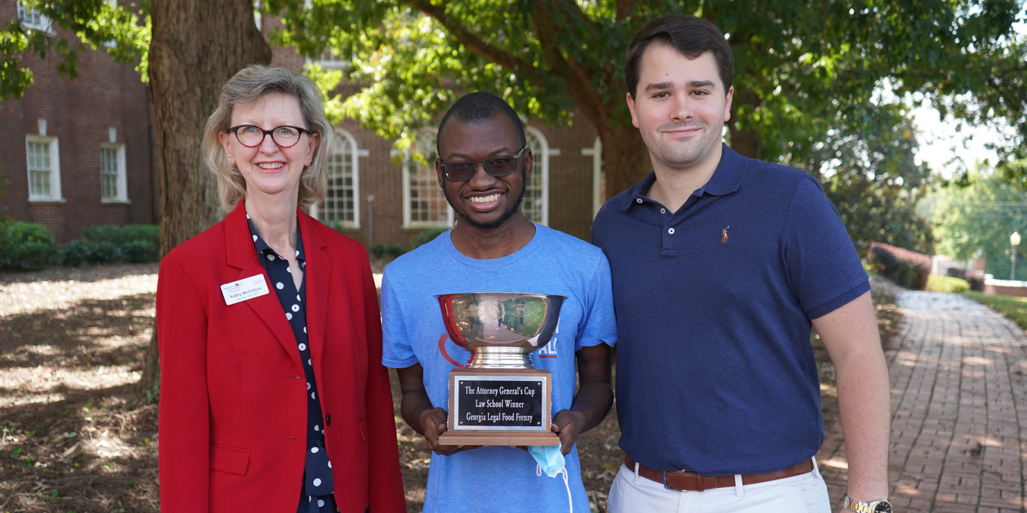 Group photo of three people holding the Attorney General's Cup trophy for Law School Food Frenzy