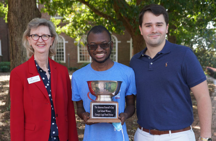 Group photo of three people holding the Attorney General's Cup trophy for Law School Food Frenzy