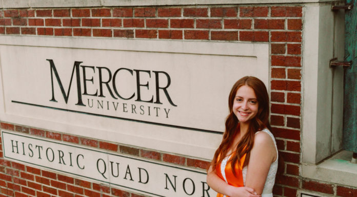 Graduate Spotlight: Anna Peerbolte A young woman wearing an orange stoll stands in front of a Mercer University sign