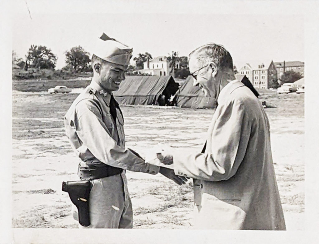 A young man dressed in an ROTC uniform shakes the hand of an older man