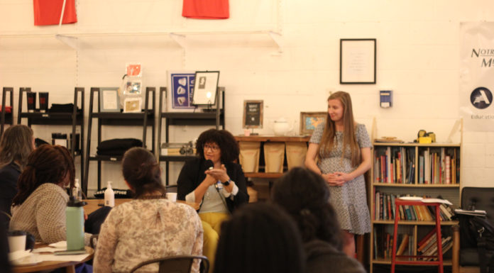 Holistic approach key to success of immigrant, refugee youth programs, Mercer study finds a woman talking into a microphone sits at a table surrounded by other people