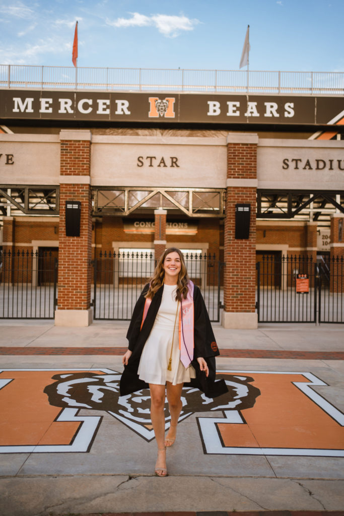 A young woman in a graduate gown stands in front of five star stadium