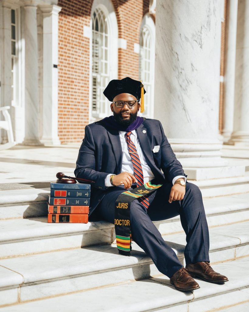 A young man wearing a suit sits on steps with law books next to him