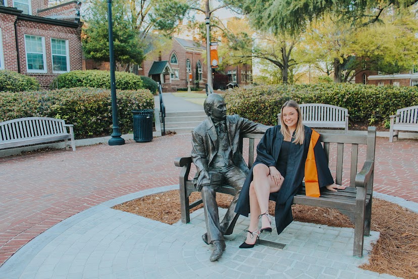A woman wearing a graduation gown sits next to a statue of Jesse Mercer