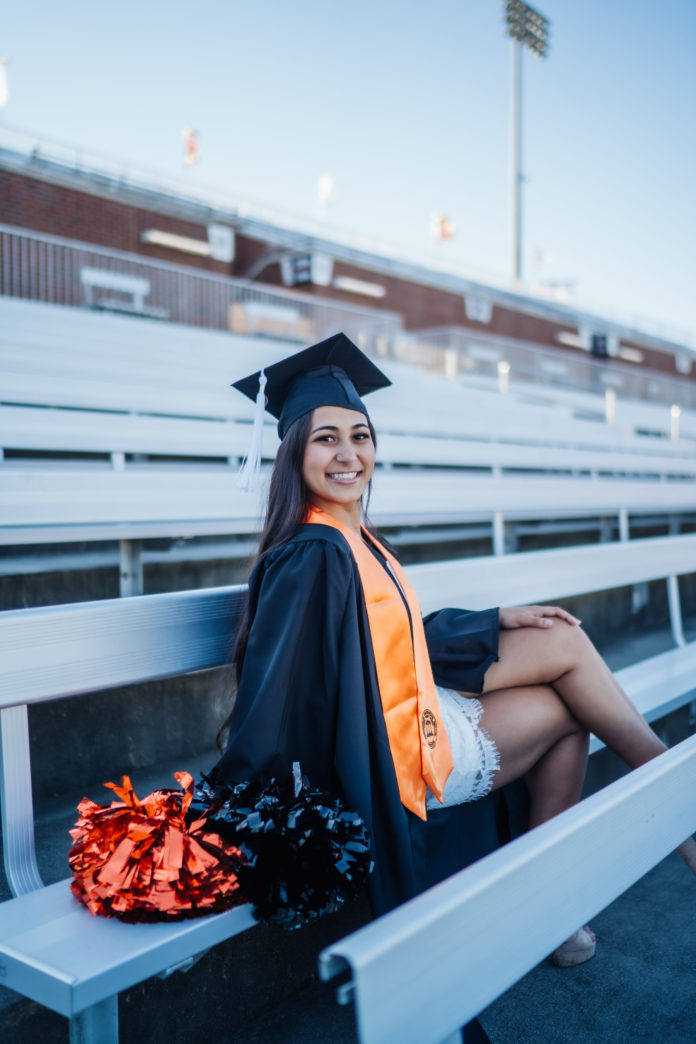 A woman sits on bleachers wearing a cap and gown