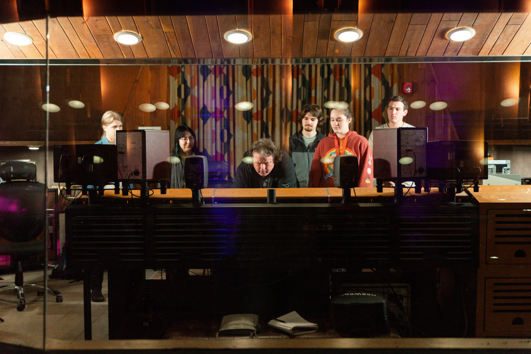 Six people gather around a sound console