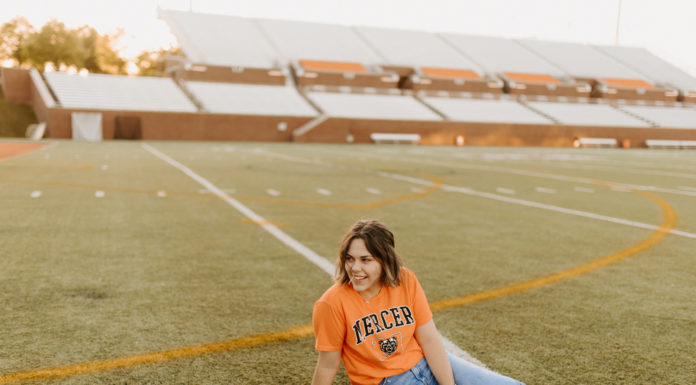 Graduate Spotlight: Olivia Cleveland A young woman wearing an orange Mercer shirt sits on a football field