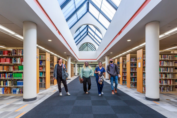 Four students walk a hallway in between shelves of books