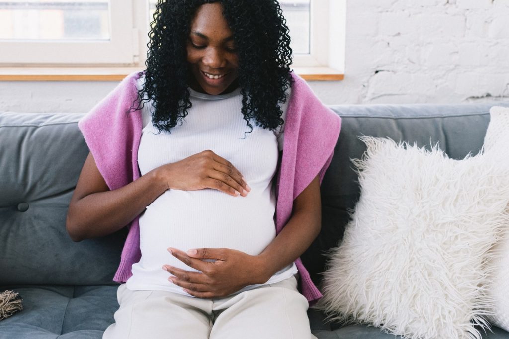 black woman on couch looks down at her pregnant belly