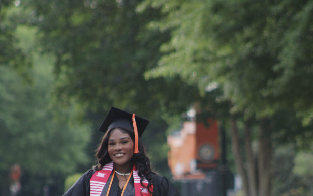Graduate Spotlight: Brittany Major A young woman wearing a graduation cap, gown and cords stands with her hands on her hips