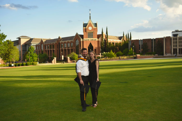 A man and woman stand in a grassy field in front of a clock tower
