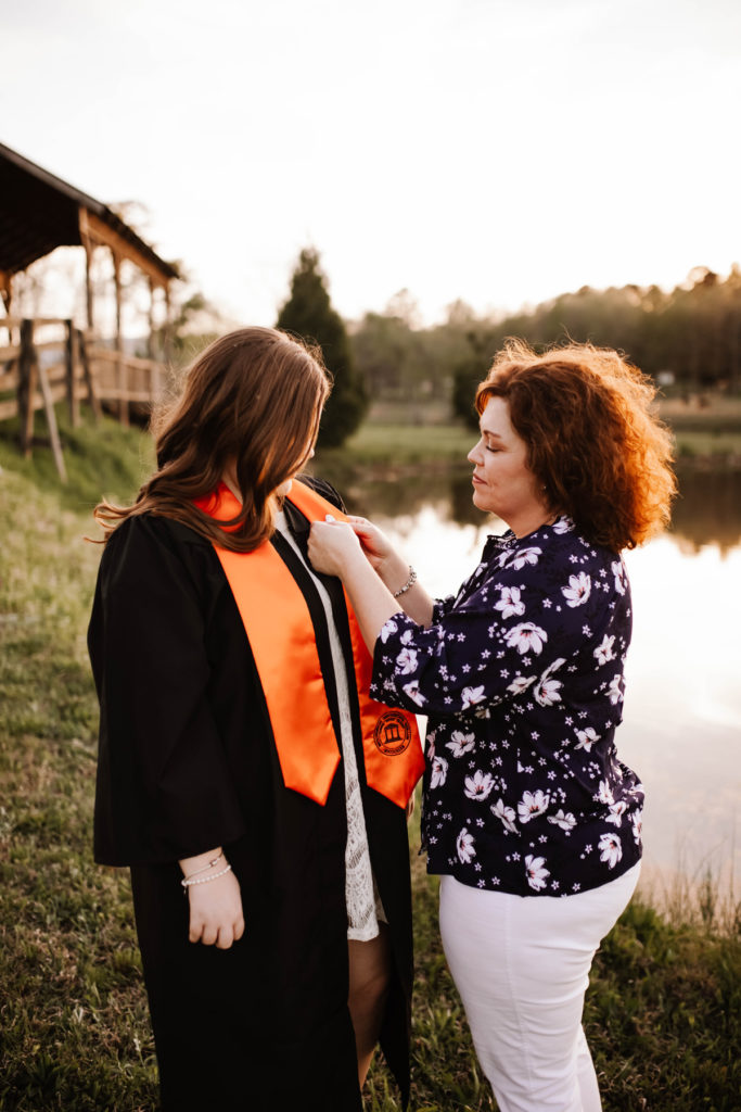 A woman places a pin on a younger woman wearing a graduation gown