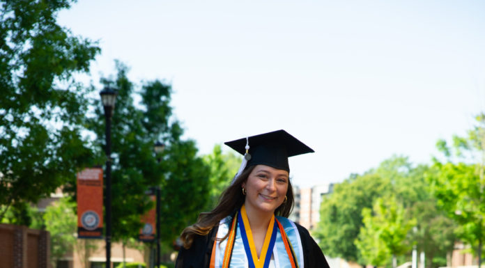 Graduate Spotlight: Maddie Runion A young woman wearing a graduation cap, gown and cords walks down a brick pathway