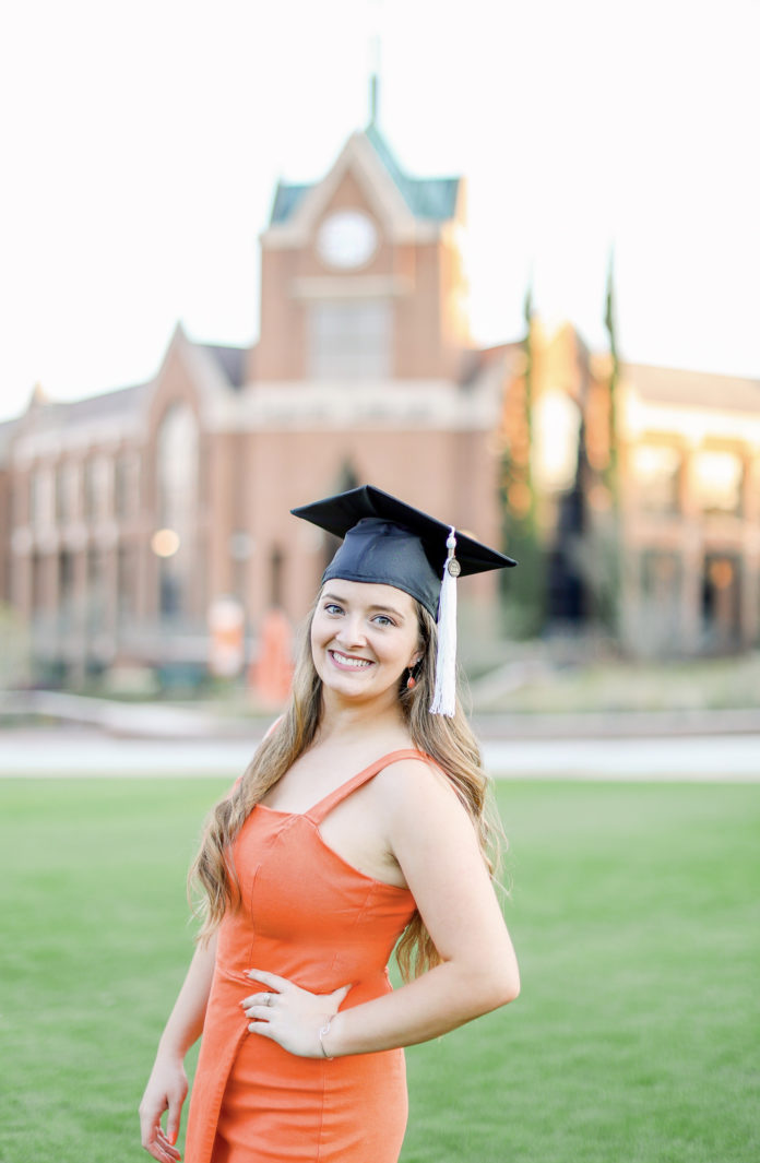A woman is wearing an orange dress and graduation cap