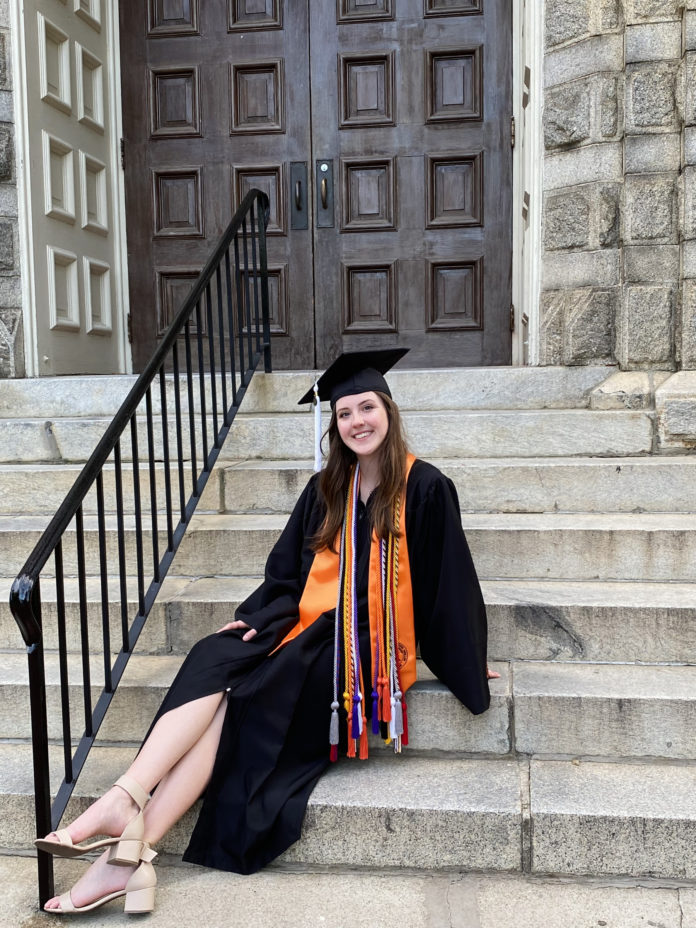 a young woman wearing a graduation cap, gown and cords sits on the steps